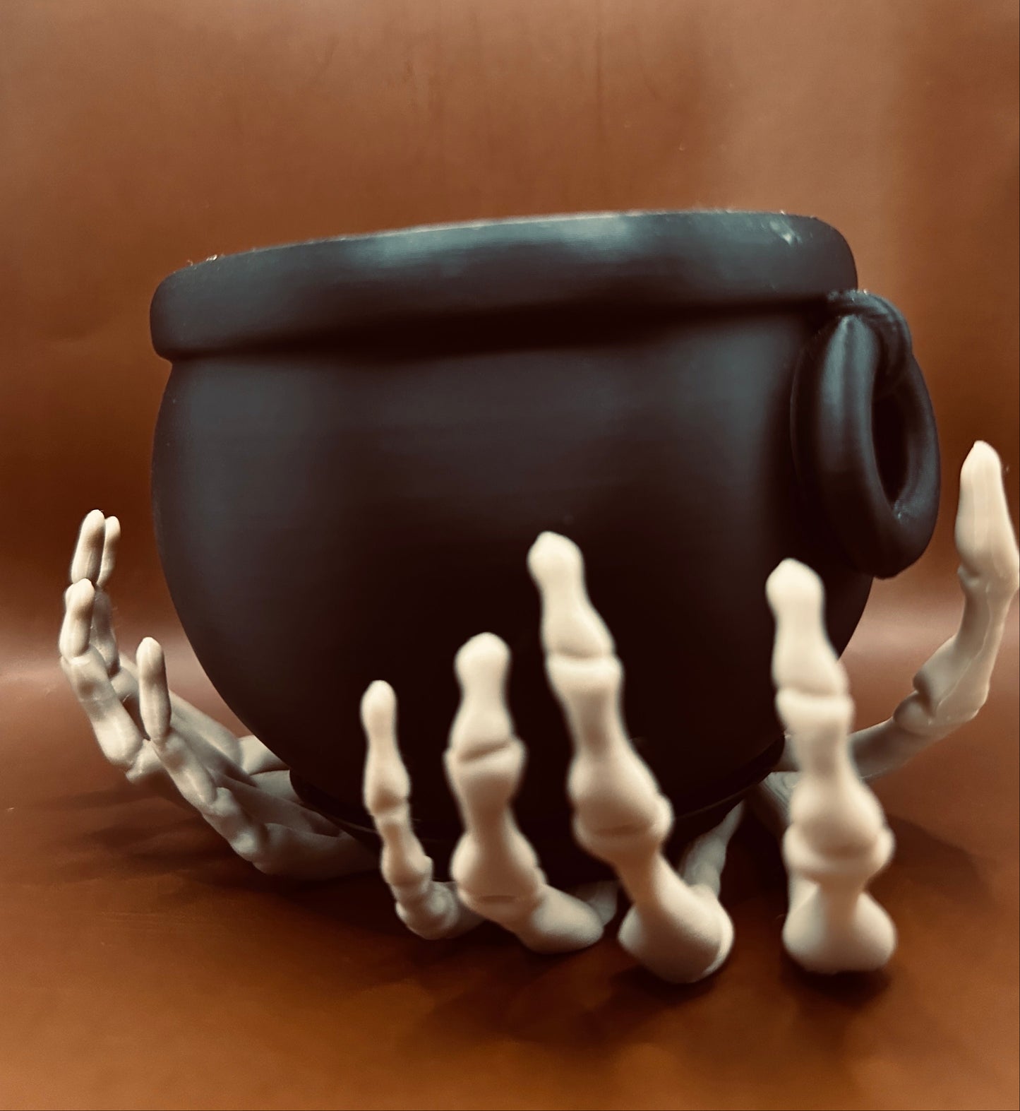Black cauldron with skeleton hands on a brown background