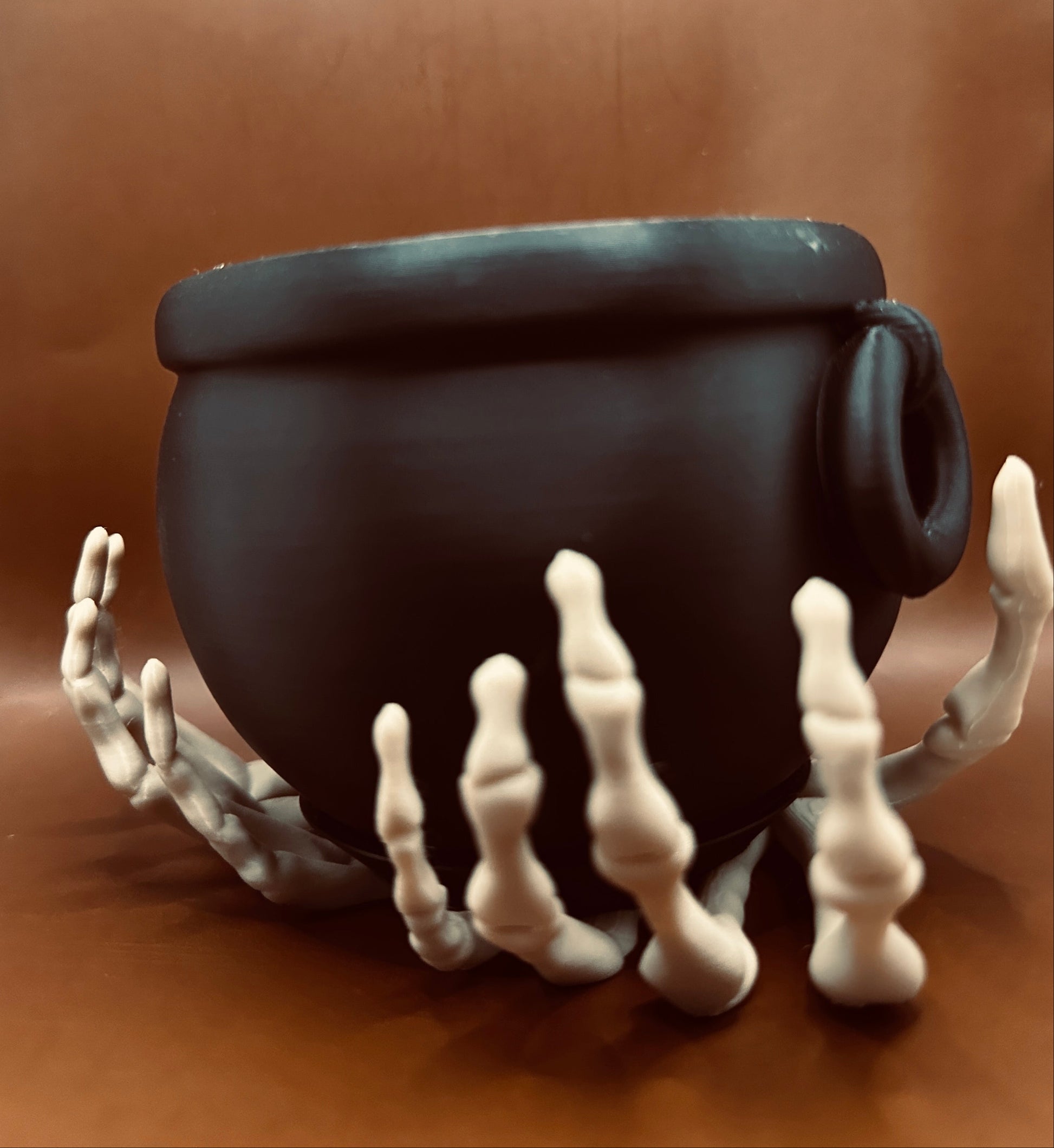 Black cauldron with skeleton hands on a brown background